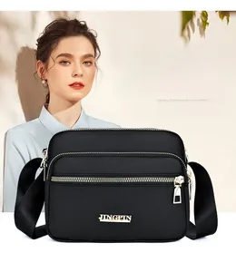 Detail of waterproof black nylon crossbody bag with multi-layer zippers and gold logo