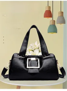 Detail of a black glossy leather handbag with a prominent gold square metal buckle