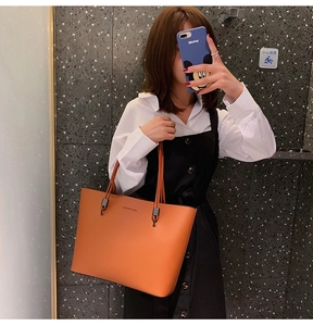 Mirror selfie showing a caramel leather tote bag with Forever Young logo and thin straps