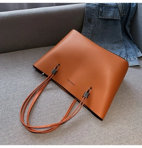 Close-up of brown leather tote bag with Forever Young text on a casual sofa setting