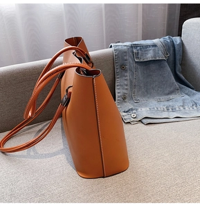 Detailed side view of orange leather tote bag showing white stitching on a gray sofa