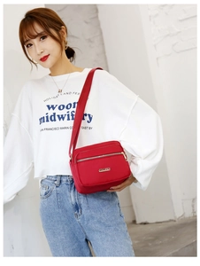 Detail of red nylon crossbody bag showing multiple zipper pockets and adjustable strap
