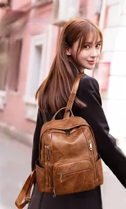 Outdoor shot of a brown soft leather backpack with multiple zip pockets on a female model