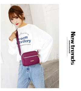 Detailed view of dark purple nylon crossbody bag with three zipper compartments and metal logo