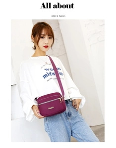 Detail view of purple nylon crossbody bag with gold JINGPIN logo on white wall