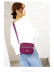 Detail showing the purple nylon crossbody bag with multi-layer zippers and gold metal hardware