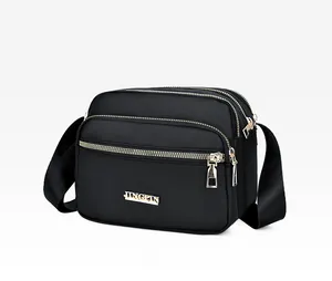 Detail view of black nylon crossbody bag featuring multi-layer gold zippers and metal logo