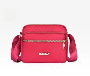 Detailed view of red nylon crossbody bag with multi-zipper layers and metallic logo