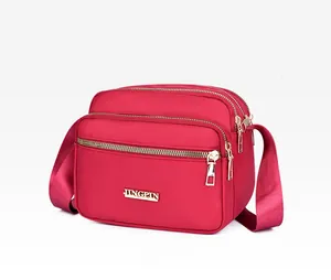 Detail view of red nylon crossbody bag with multiple zip pockets and gold metal logo