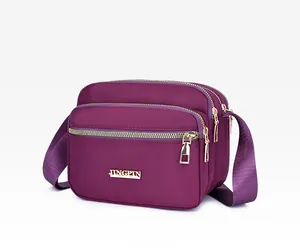 Detail view of purple nylon crossbody bag featuring three-tier zipper pockets and gold hardware