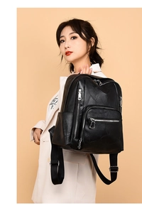 Detail of a black quilted leather backpack with silver zippers on a model's back