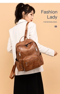 Detail view of stylish brown leather backpack with multiple metal zippers worn by model