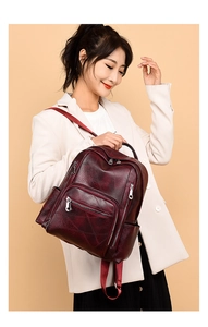Detail view of burgundy leather backpack featuring geometric quilting and multi-zipper pockets