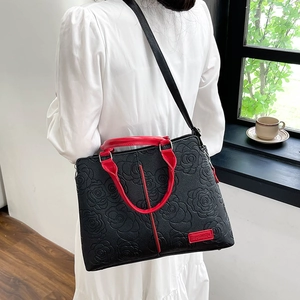 Detailansicht der schwarzen Handtasche mit roten Griffen und Rosenprägung auf dem Leder
