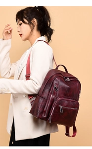 Side view of wine red leather backpack with multiple zipper pockets on female model