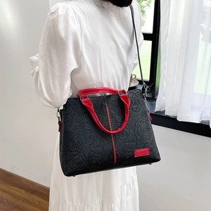 Detail einer floral geprägten schwarzen Ledertasche mit roten Riemen und Struktur