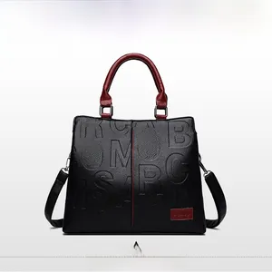 Details der schwarzen Handtasche aus Leder mit dunkelroten Griffen und Reliefbuchstaben