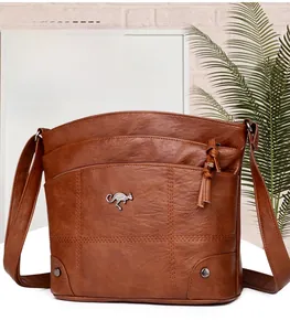 Détail d'un sac bandoulière en cuir marron avec logo kangourou en métal et pompon zippé