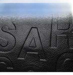 Detail der schwarzen Handtasche aus Narbenleder mit geprägter SAF-Schrifttextur