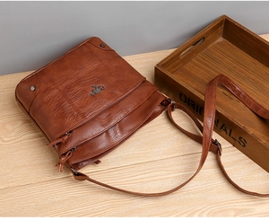 Détail du sac bandoulière en cuir marron foncé avec logo en métal et multiples fermetures