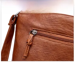 Détail du sac en cuir marron à motif litchi montrant la poche zippée et la tirette nouée