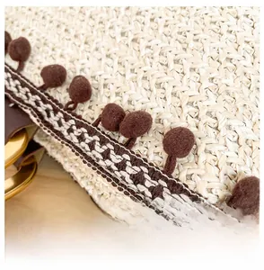 Detailed macro view of woven straw tote bag with brown pom-poms and bohemian trim