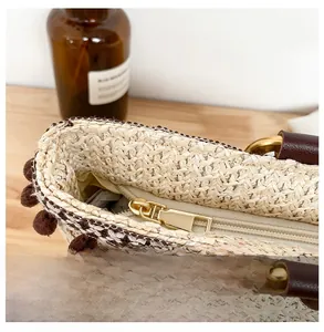 Detailed macro view of woven straw bag featuring gold zipper and brown tassel pom-poms