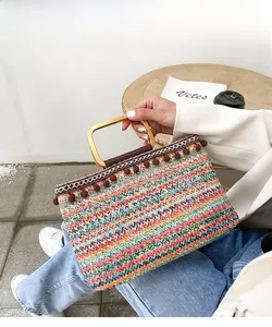 Detail of colorful woven straw bag featuring pom-poms and square golden metal handles
