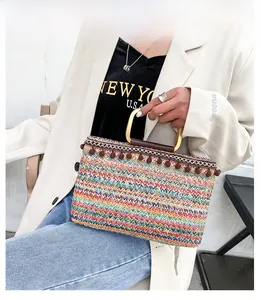 Detail of colorful woven straw tote bag with brown pompom tassels and golden metal handle