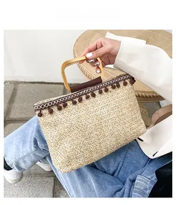 Detail of straw tote bag with brown pom-pom trim and golden square metal handles