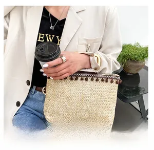 Detail of straw woven handbag with brown pom-pom charms and wooden handle in a lifestyle setting