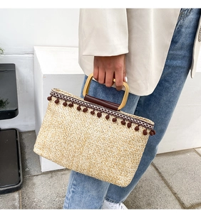 Detail of straw woven tote bag with dark brown pom-poms and ethnic geometric ribbon