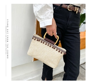 Detail of straw tote bag with golden U-shaped handle and brown pompom tassel accent