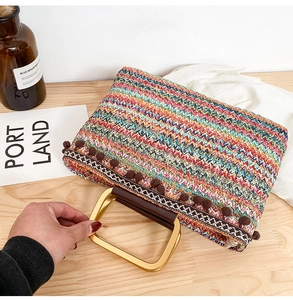 Detail of colorful woven straw handbag with brown pom-pom tassels and gold metal handle