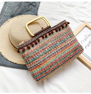 Detail of colorful woven straw tote bag with gold metal handle and brown pom-pom trim