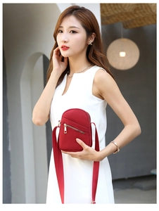 Close-up of a red nylon crossbody phone bag with multi-layer zippers and wide strap