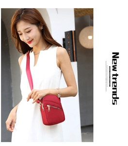 Red nylon crossbody bag with multi-layer zippers worn by a model in a modern space