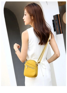 Adjustable textile strap and diagonal zipper detail on a bright yellow crossbody bag
