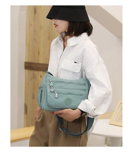 Close-up of a mint green nylon crossbody bag with multiple functional zipper compartments