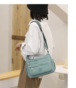 Close-up of a light blue nylon crossbody bag featuring multiple front zipper pockets