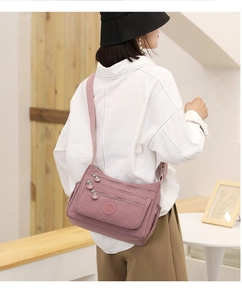 Detail view of pink nylon crossbody bag with multiple zip pockets and adjustable strap