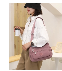 Detail of mauve nylon crossbody bag with multiple zippers and adjustable strap on a model