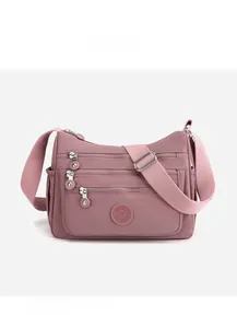 Detail view of pink nylon crossbody bag with multiple zip compartments and side pockets