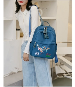 Gros plan d'un sac à dos bleu marine avec broderie de cerf porté par un mannequin chic