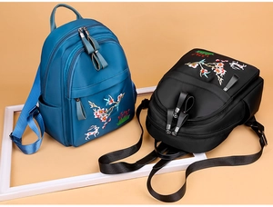 Détail de broderies fleurs et cerfs sur des sacs à dos en nylon bleu et noir