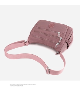 Detail view of pink nylon crossbody bag with multiple zip pockets and metal hardware