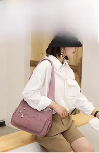 Detailed side view of mauve nylon crossbody bag with multi-zipper pockets on a model