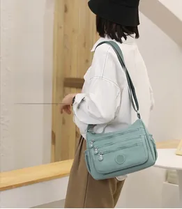Detailed side view of light green nylon crossbody bag with multiple zipper compartments