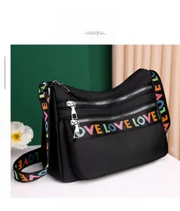 Detail of black nylon crossbody bag featuring colorful LOVE embroidered strap and zippers