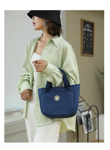 Détail d'un sac cabas en nylon bleu marine avec logo porté par un mannequin en tenue décontractée